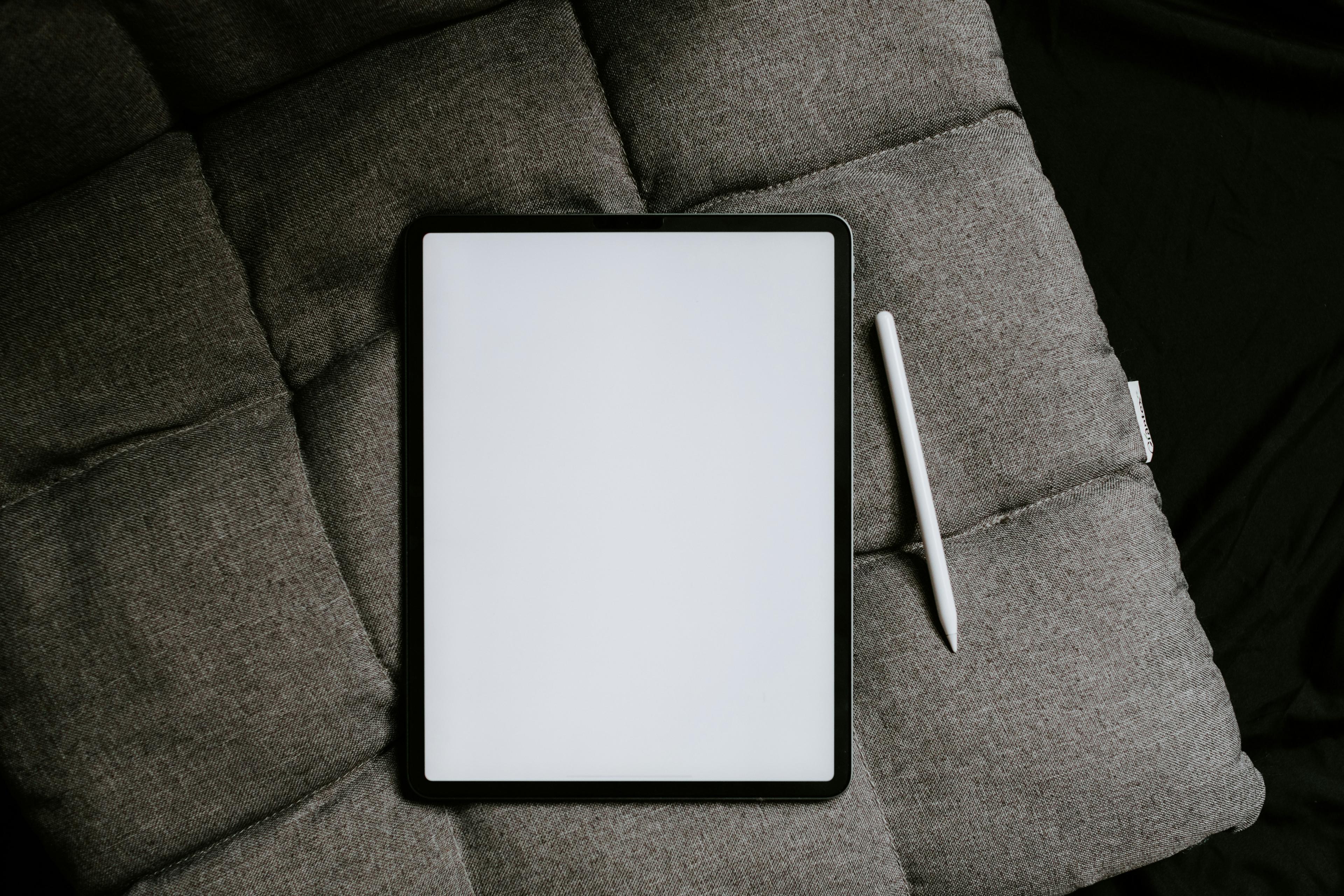 iPad with white screen on corner of grey couch.
